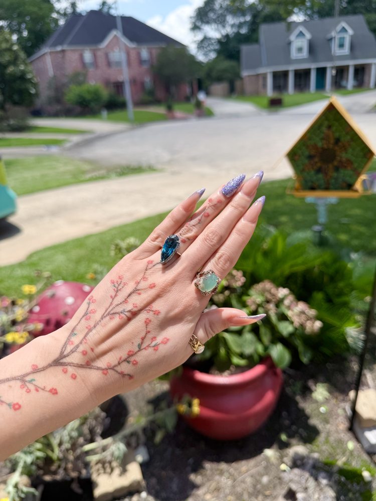 Delicate fine-line cherry blossom branch trailing across the back of a hand