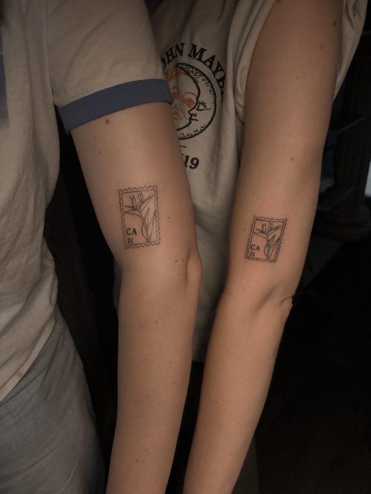 Matching fine-line postage-stamp tattoos of a bird-of-paradise flower