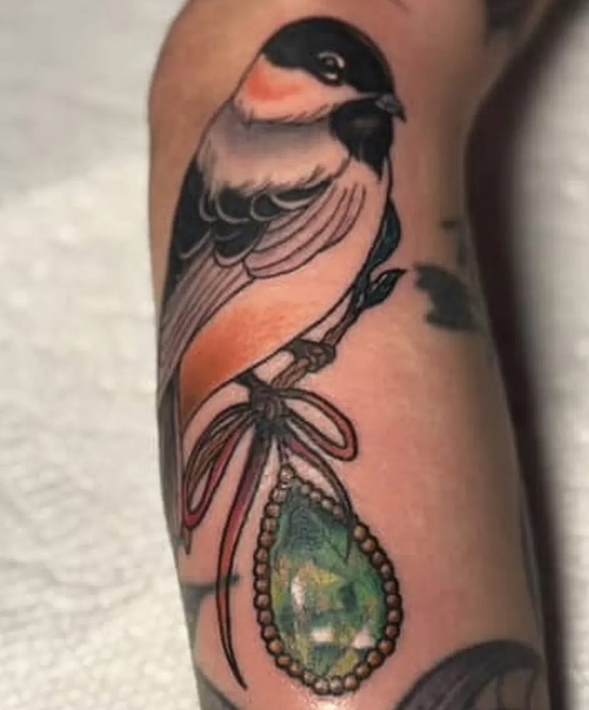 Songbird perched on a ribbon holding a green crystal pendant